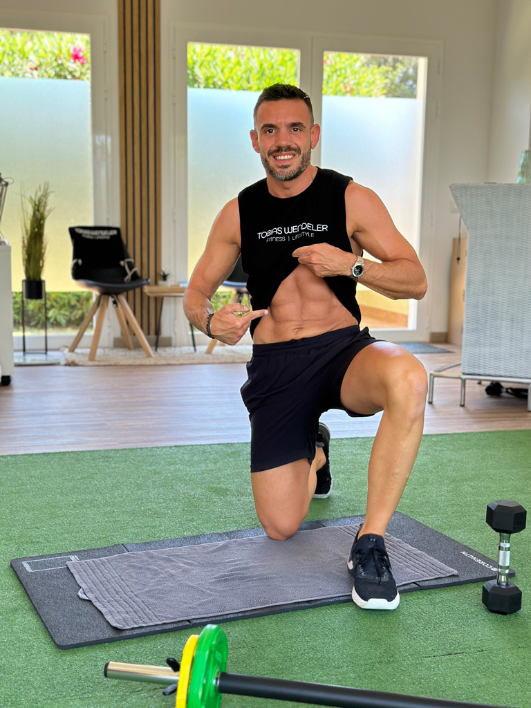 Coach kniet auf einem Knie und zeigt definierte Bauchmuskeln.